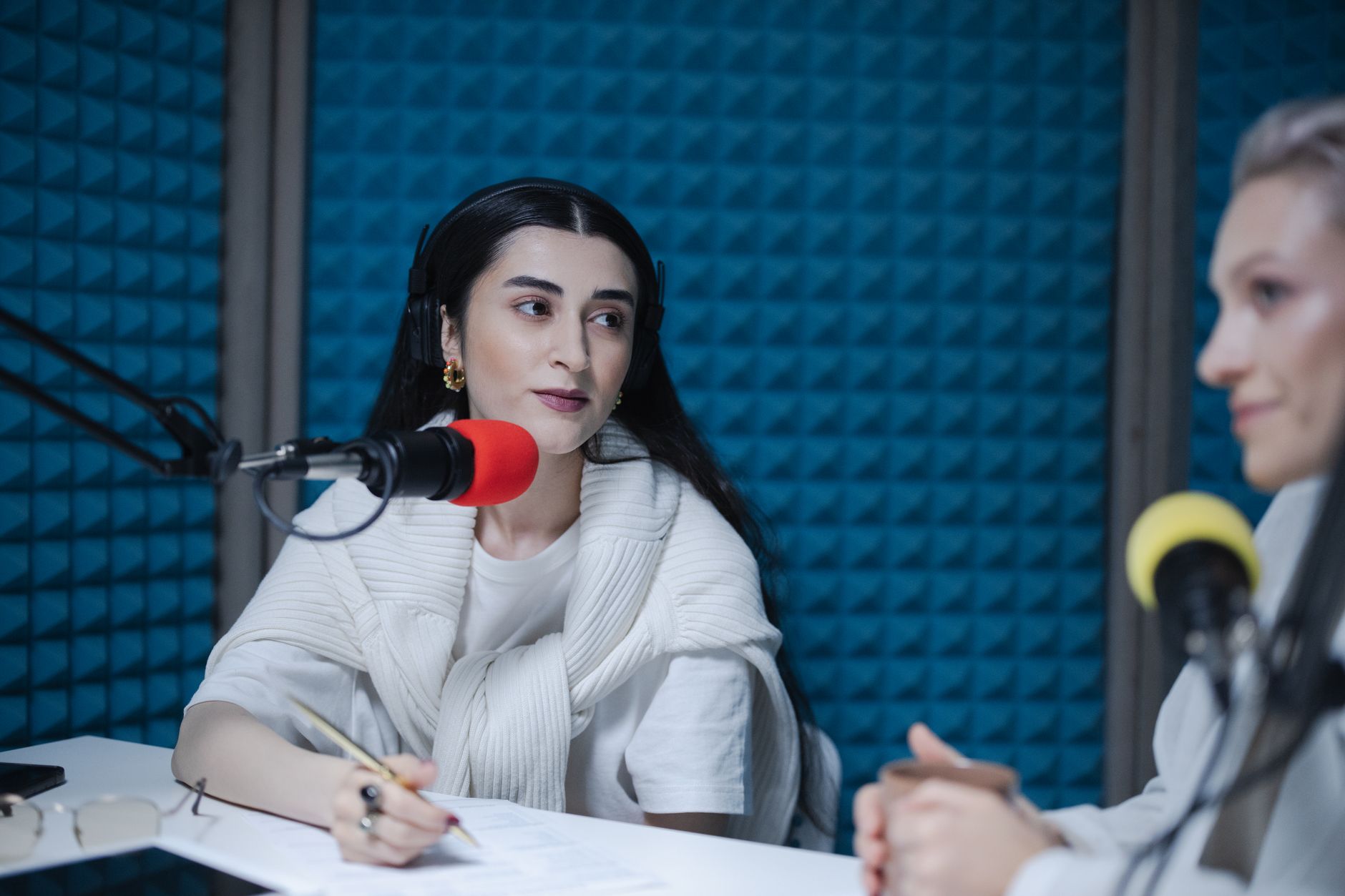 Suno AI Review 2026: Can This AI Music Generator Create Real Indian Songs? Two women engaged in a podcast recording with professional microphones, soundproof studio.