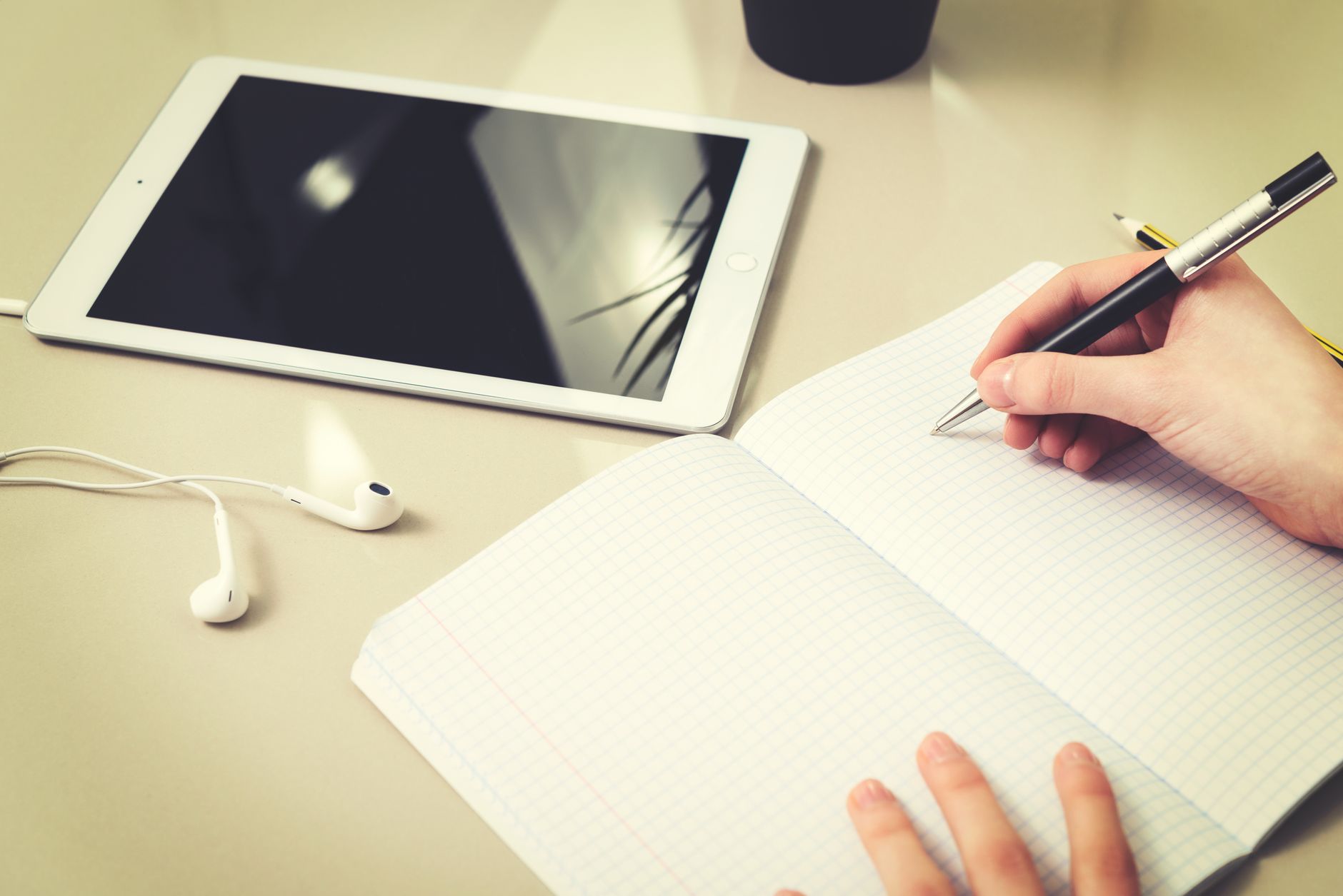 Student writing notes beside tablet and earphones for digital study