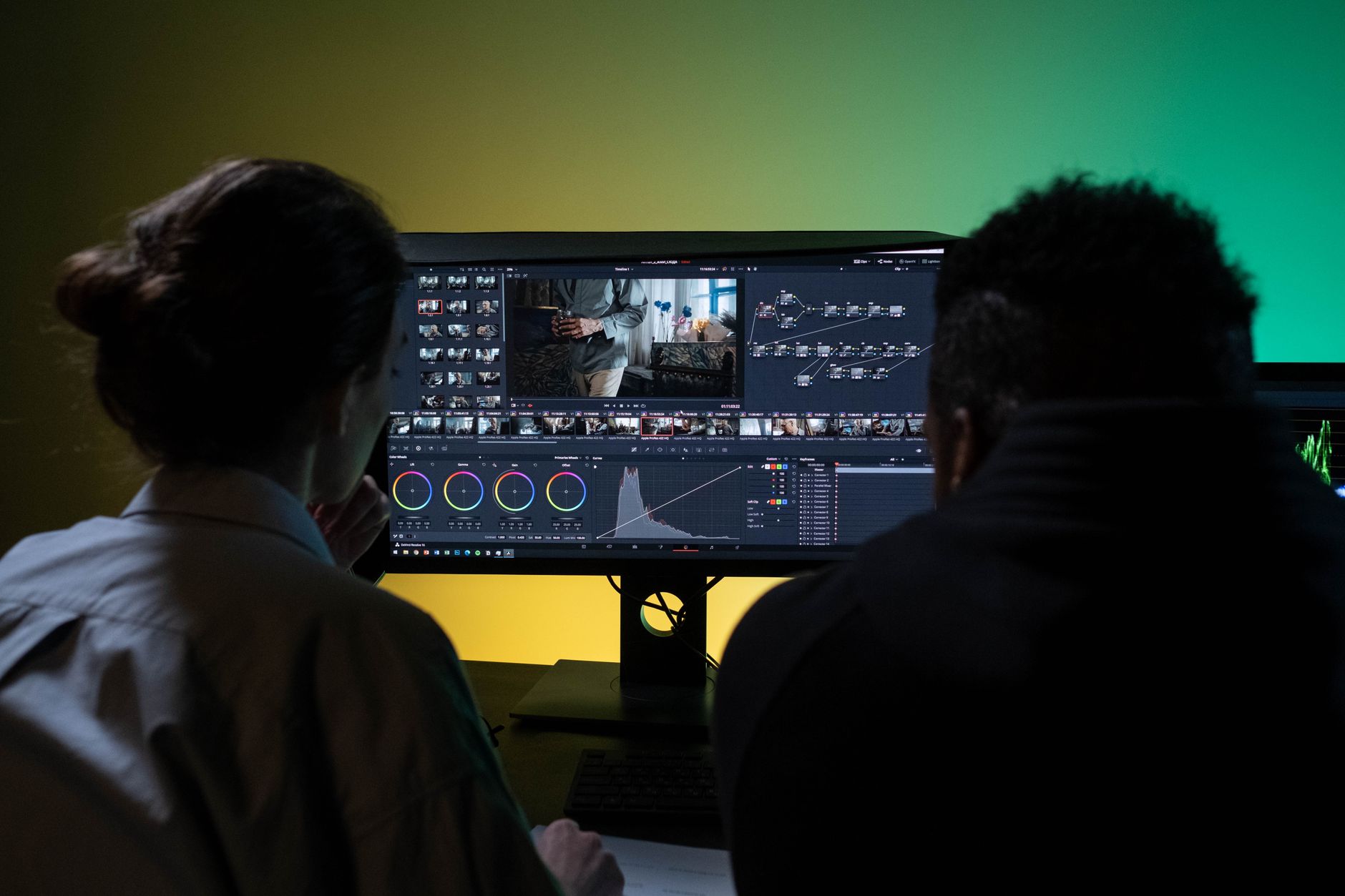 Two professionals video editing on dual monitors in modern workspace