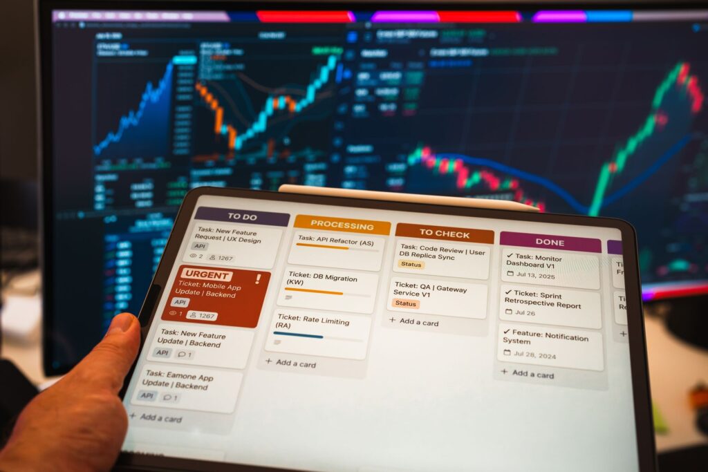 Tablet with business task management app in front of stock chart monitors.