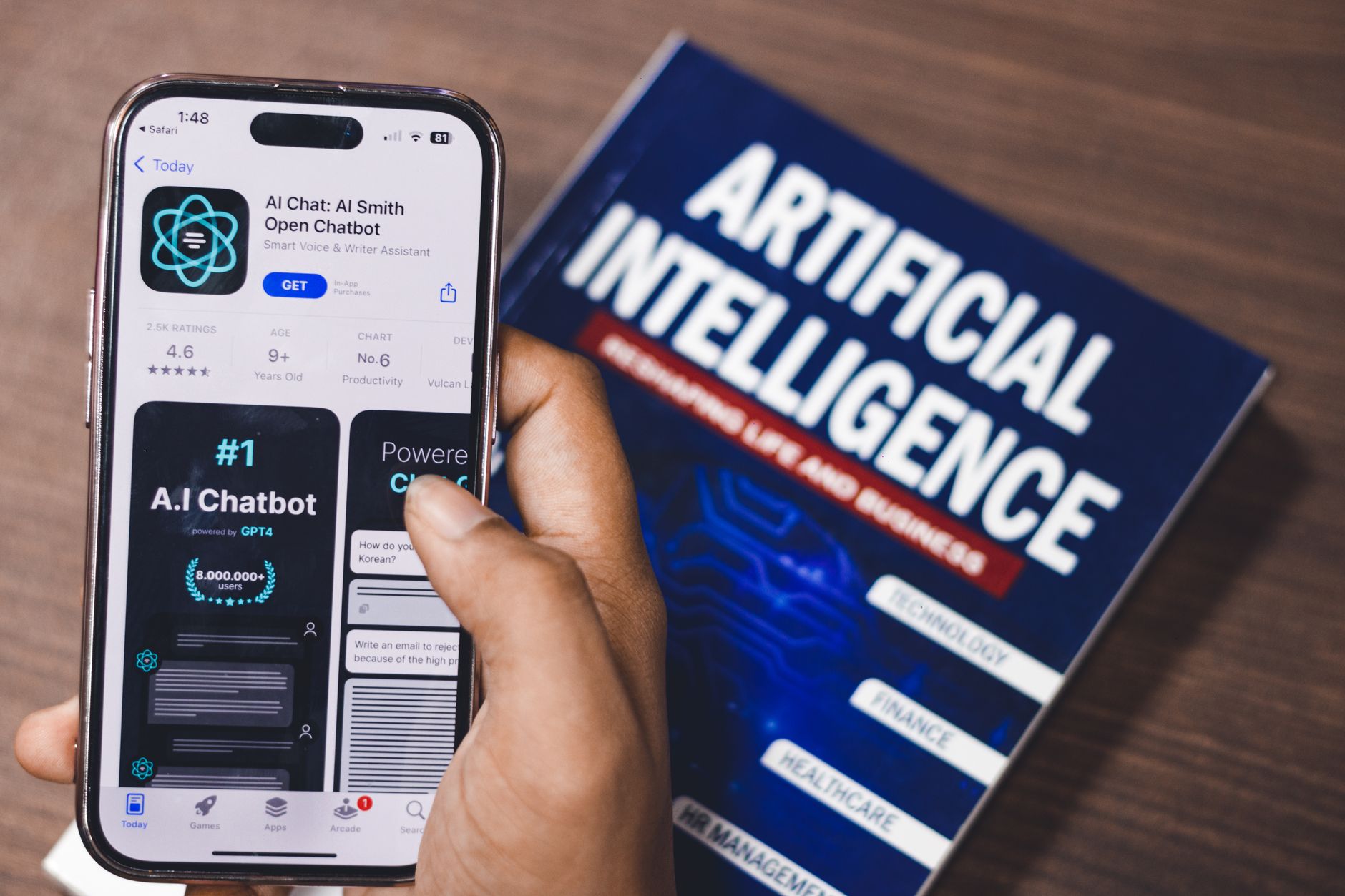 Smartphone showing AI chatbot app alongside an Artificial Intelligence book on desk